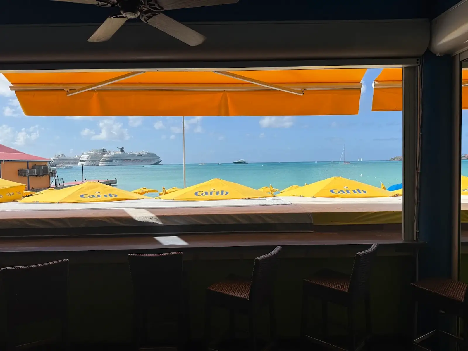 A cruise ship anchored in Great Bay viewed from the bar at Thirsty Pirate over rows of yellow Carib beach umbrellas in Philipsburg