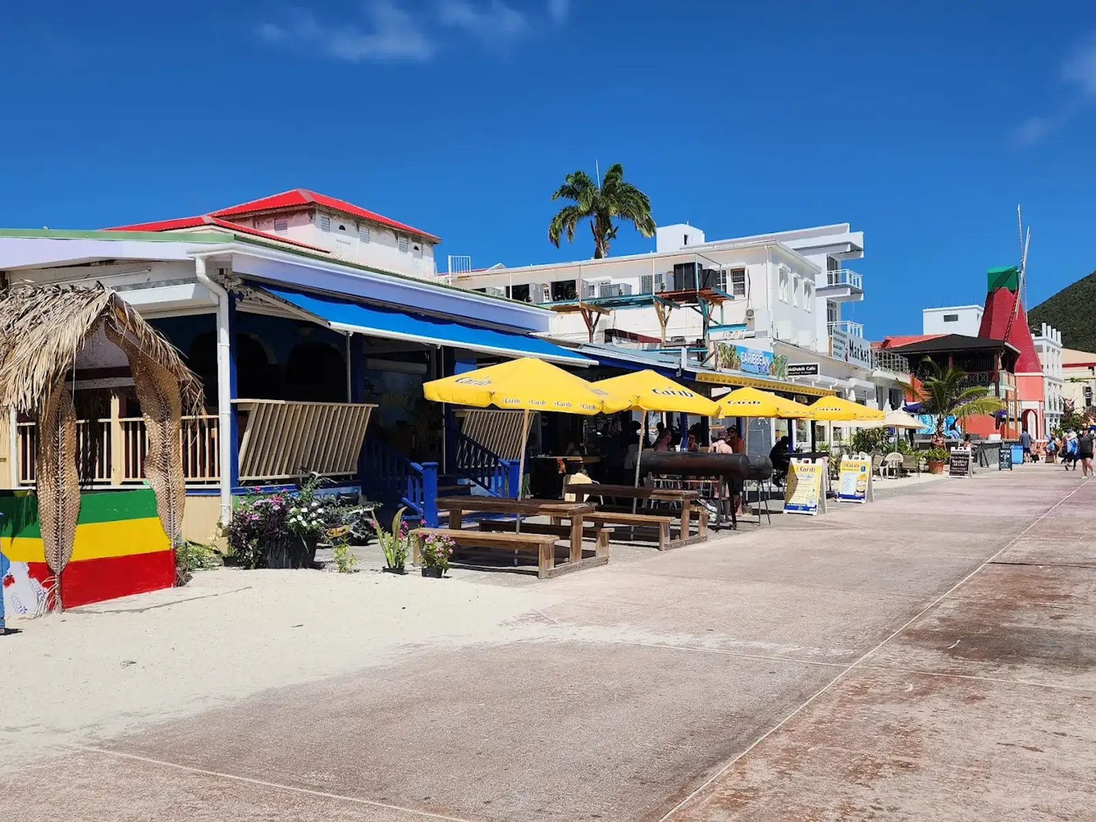 Thirsty Pirate Beach Bar on the Philipsburg boardwalk with yellow Carib umbrellas, palm shade and a clear blue Caribbean sky in Sint Maarten